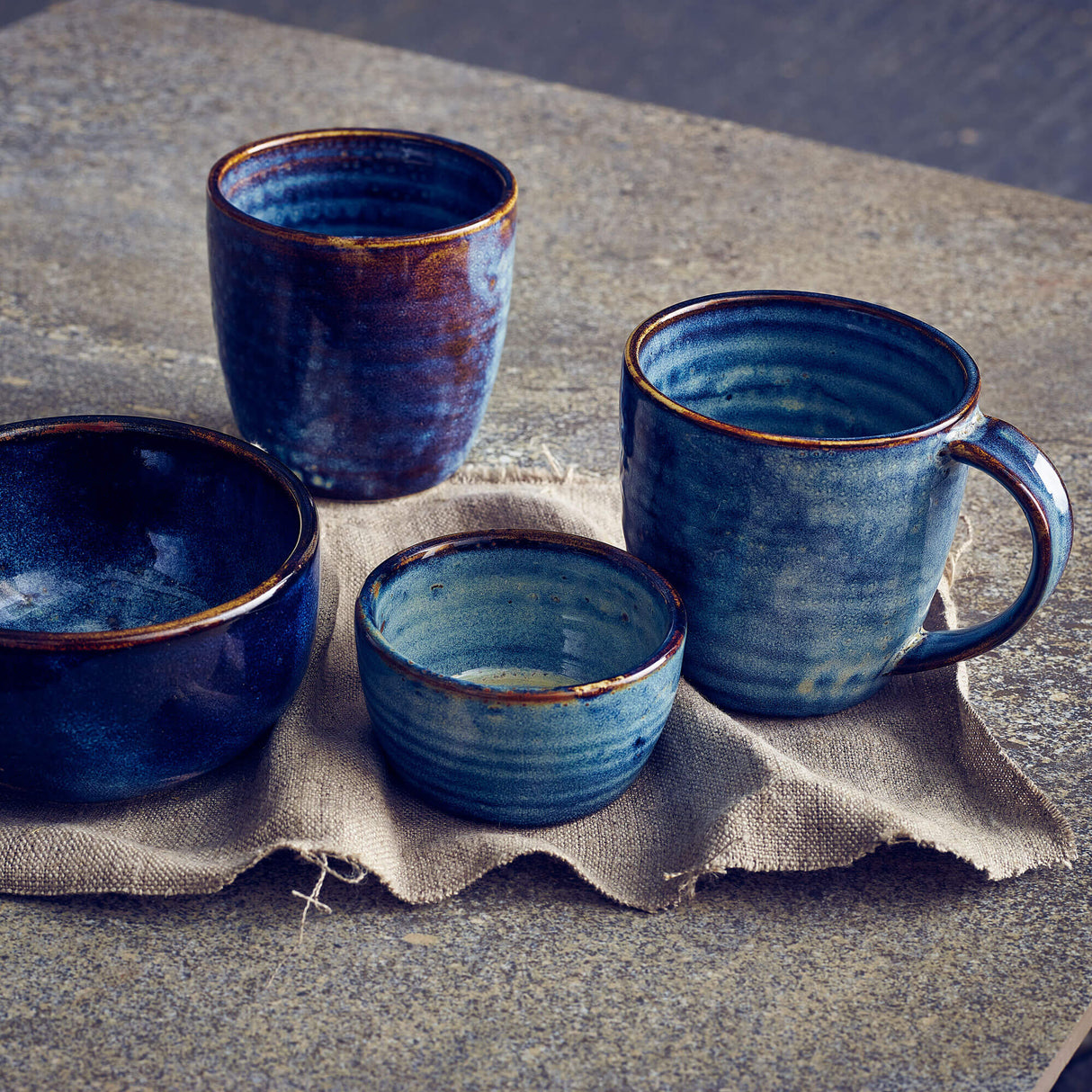Set of blue ceramic mugs and bowls on a textured surface