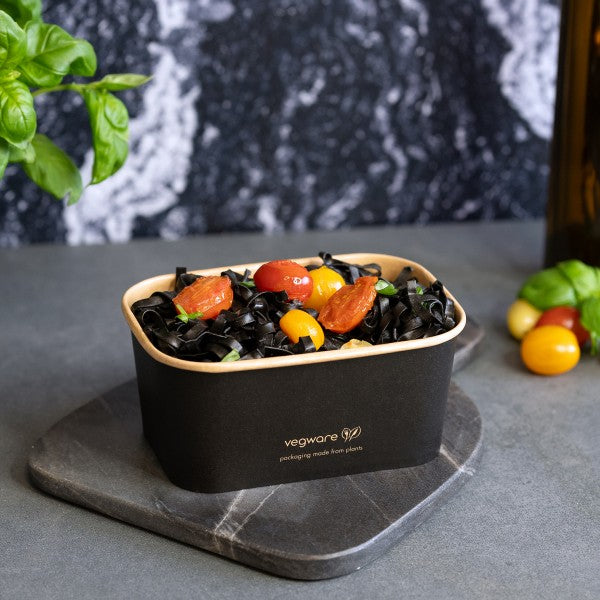 Black and beige container with salad on a gray surface, featuring Vegware branding.