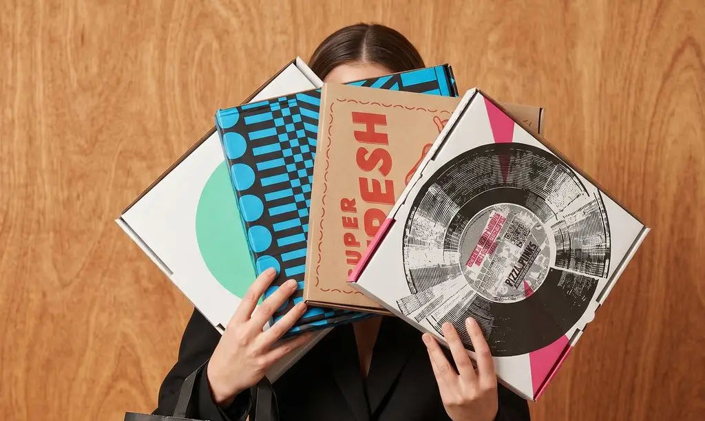 Person holding vinyl records with colorful covers on a wooden surface