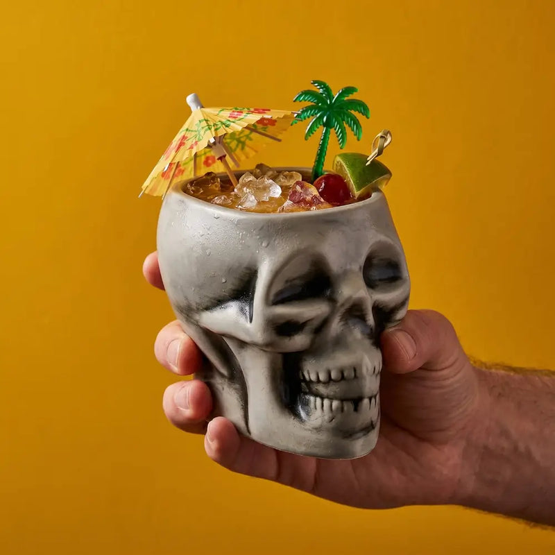 Skull-shaped cocktail glass with a tropical drink on a yellow background
