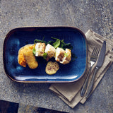 Blue plate with a dish of food on a gray surface with a napkin and cutlery.