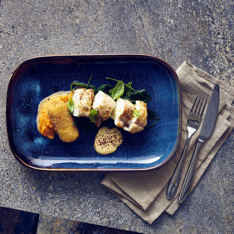 Blue plate with a dish of food on a gray surface with a napkin and cutlery.
