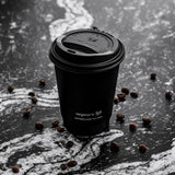Black Vegware coffee cup on a dark surface with scattered coffee beans