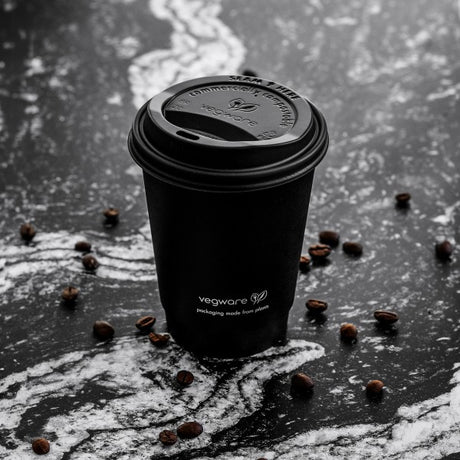 Black Vegware coffee cup on a dark surface with scattered coffee beans