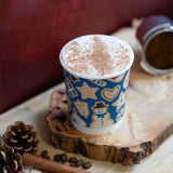 Hot chocolate in a blue cup with gingerbread men design on a wooden surface.
