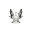 A clear glass with a Tiki-style head design, featuring a happy face on one side and a sad face on the reverse side, with a footed base.