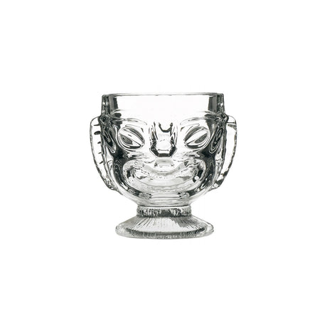 A clear glass with a Tiki-style head design, featuring a happy face on one side and a sad face on the reverse side, with a footed base.