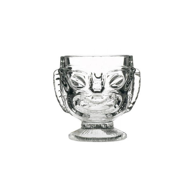 A clear glass with a Tiki-style head design, featuring a happy face on one side and a sad face on the reverse side, with a footed base.