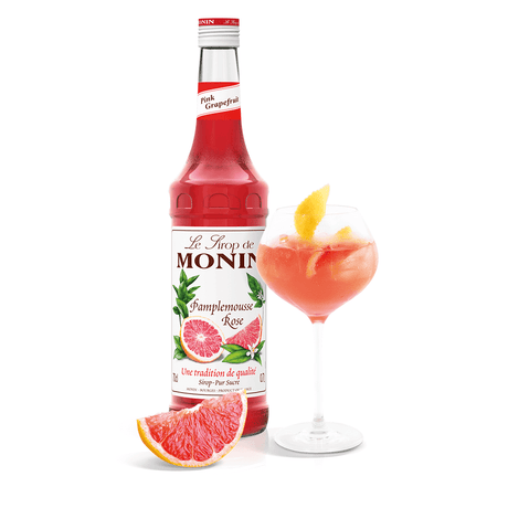 bottle of monin grapefruit syrup beside a gin glass