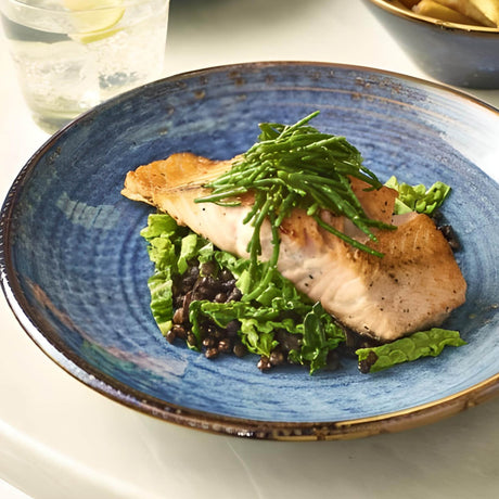 Blue plate with fish and greens on a white surface
