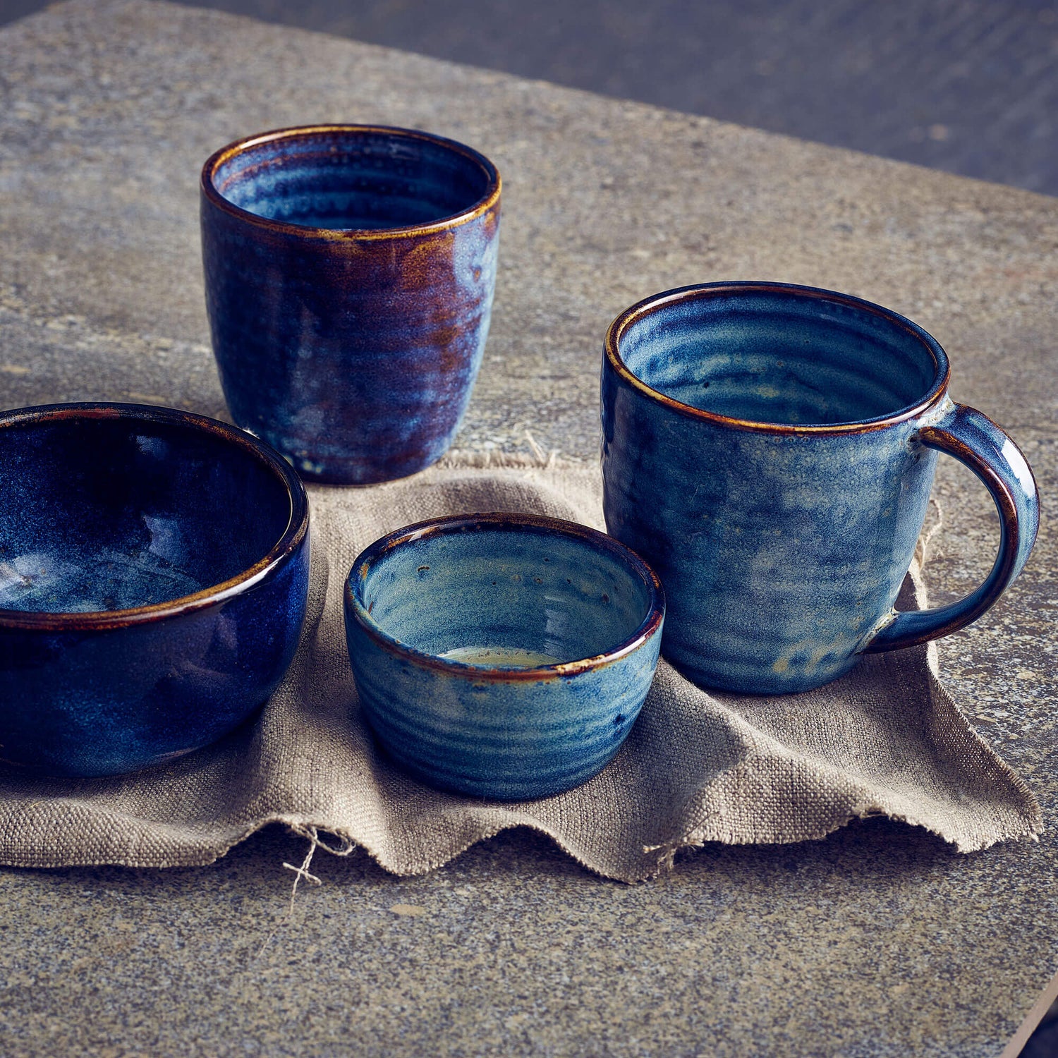 Set of blue ceramic mugs and bowls on a textured surface