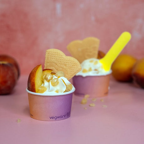 Ice cream cups with cookies and a yellow spoon on a pink background