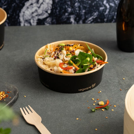 Colorful salad in a black vegware container on a gray surface with a blurred background