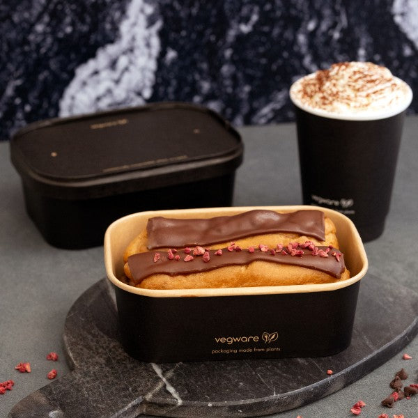 Eclair with chocolate topping and red berries in a black Vegware container on a dark surface.