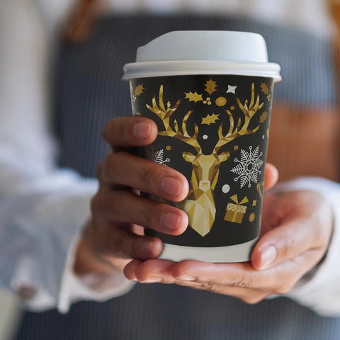 Person holding a festive coffee cup with reindeer and snowflake design.